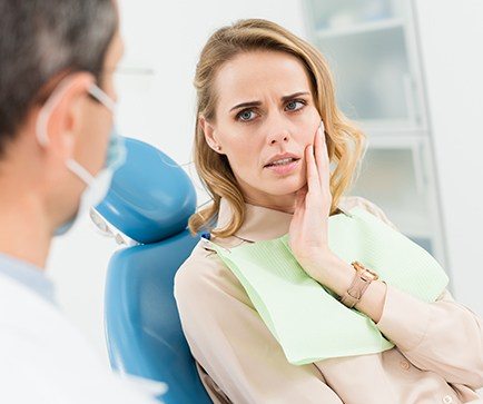 Woman in dental chair holding cheek