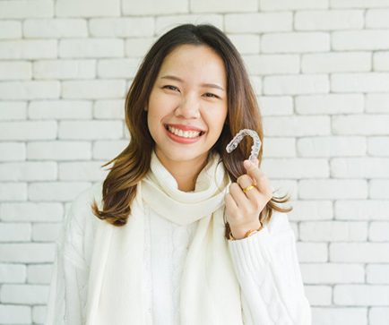 woman in white sweater holding Invisalign tray